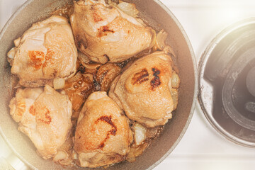 Fried juicy chicken in a frying pan, cooked on an electric stove in the kitchen. The view from the top. Meat fat food.