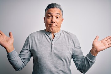 Middle age handsome grey-haired man wearing casual t-shirt over white background clueless and confused expression with arms and hands raised. Doubt concept.