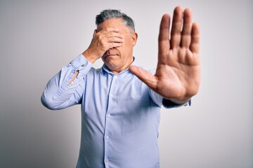 Middle age handsome grey-haired business man wearing elegant shirt over white background covering eyes with hands and doing stop gesture with sad and fear expression. Embarrassed and negative concept.