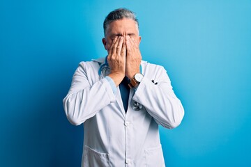 Middle age handsome grey-haired doctor man wearing coat and blue stethoscope rubbing eyes for fatigue and headache, sleepy and tired expression. Vision problem