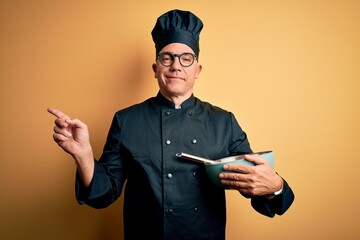 Middle age handsome grey-haired chef man wearing cooker uniform and hat using whisk very happy...