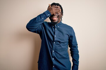 Fototapeta premium Young handsome african american man wearing casual shirt standing over white background smiling and laughing with hand on face covering eyes for surprise. Blind concept.
