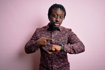 Young handsome african american man wearing casual shirt standing over pink background In hurry pointing to watch time, impatience, upset and angry for deadline delay