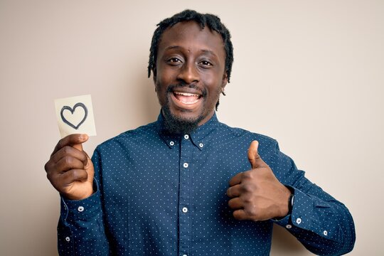 African american romantic man holding reminder with heart symbol over white background happy with big smile doing ok sign, thumb up with fingers, excellent sign