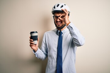 Young businessman wearing glasses and bike helmet drinking cup of coffee with happy face smiling doing ok sign with hand on eye looking through fingers