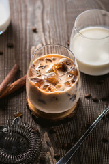 Ice coffee with cream poured over and coffee beans on a old rustic wooden table