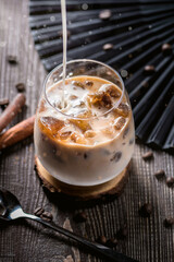 Ice coffee with cream poured over and coffee beans on a old rustic wooden table