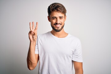 Young handsome man with beard wearing casual t-shirt standing over white background showing and...