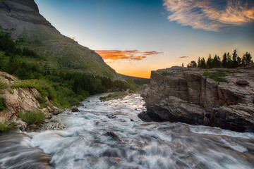 Beautiful dawn over mountain stream. Orange clouds are on blue sky.  Location place is Swiftcurrent...