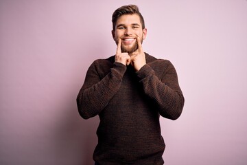 Young blond man with beard and blue eyes wearing casual sweater over pink background Smiling with open mouth, fingers pointing and forcing cheerful smile