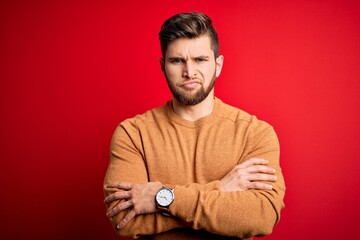 Young blond man with beard and blue eyes wearing casual shirt over red background skeptic and nervous, disapproving expression on face with crossed arms. Negative person.