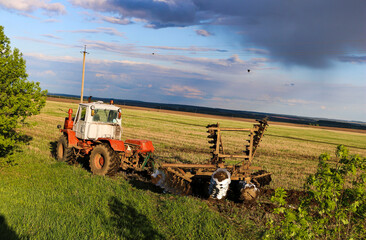  tractor plows and harrows  land in  large field on  sunny spring day. preparing  soil for planting...