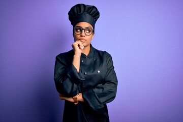 Young african american chef girl wearing cooker uniform and hat over purple background with hand on chin thinking about question, pensive expression. Smiling with thoughtful face. Doubt concept.