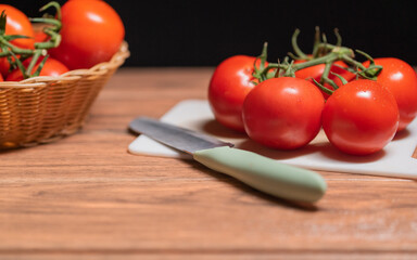 White cutting board with fresh red tomatoes and a knife perched on the left side on a brown table