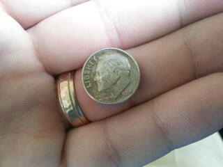 silver dime in hand with gold wedding ring - obrazy, fototapety, plakaty
