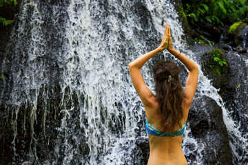 Close up of yoga woman raising arms with namaste mudra in front of waterfall. View from back. Pucak Manik waterfall Wanagiri, Bali, Indonesia.