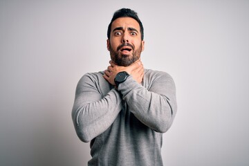 Young handsome man with beard wearing casual sweater standing over white background shouting and suffocate because painful strangle. Health problem. Asphyxiate and suicide concept.