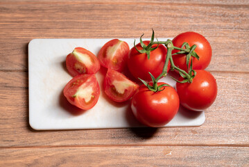 Ripe red tomatoes on white chopping board with many piece of chopped tomatoes on brown wooden table