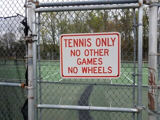 tennis only no other games no wheels sign on metal fence at tennis court
