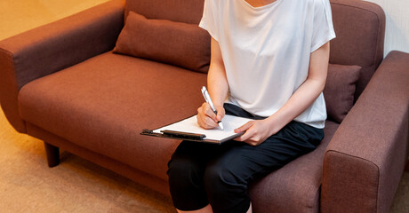 エステサロンやクリニックの受付のソファで問診票を書き込む女性