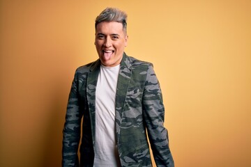 Fototapeta premium Young handsome modern man wearing business jacket standing over yellow isolated background sticking tongue out happy with funny expression. Emotion concept.