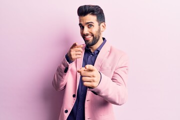 Young handsome man with beard wearing elegant jacket pointing fingers to camera with happy and funny face. good energy and vibes.
