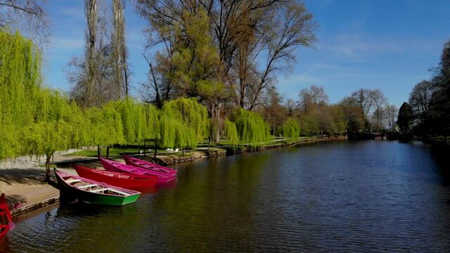 Paradise tranquil park with anchored boats on bank of canal under green willows on a sunny spring day