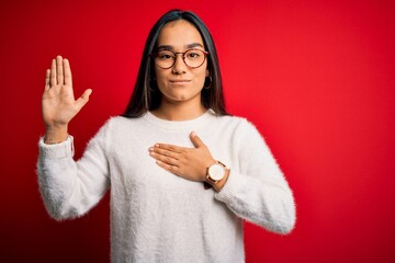 Young beautiful asian woman wearing casual sweater and glasses over red background Swearing with...