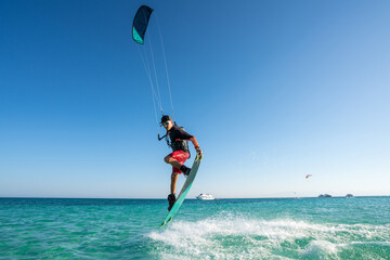 kiter does a difficult trick on a background of transparent water and blue sky