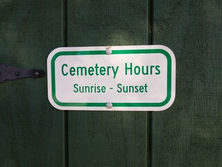 cemetery hours sunrise to sunset sign on green wood