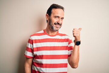 Middle age hoary man wearing casual striped t-shirt standing over isolated white background smiling with happy face looking and pointing to the side with thumb up.