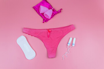 Women's panties with menstrual cups, sanitary pads and tampons on pastel pink background. Top view. Concept of critical days, menstruation, feminine hygiene