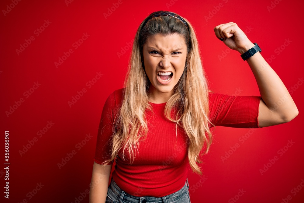 Poster young beautiful blonde woman wearing casual t-shirt standing over isolated red background angry and 