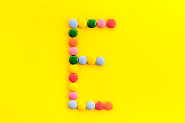 Letter E - alphabet made with sweets on yellow from above