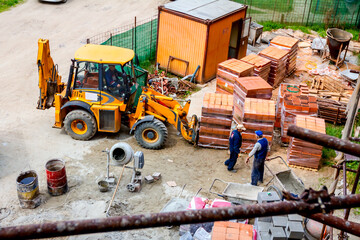 Excavator is working as forklift for delivery transport pack of red blocks on wooden pallet