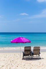 Beach chairs under pink umbrella on sand beach with beautiful blue sea and clear blue sky view, relaxing by the beach, summer outdoor day light, holiday break