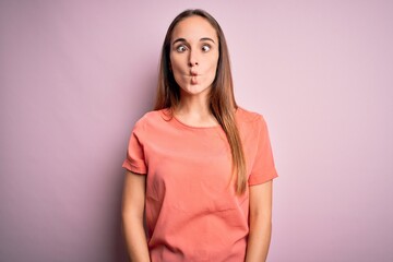 Young beautiful woman wearing casual t-shirt standing over isolated pink background making fish face with lips, crazy and comical gesture. Funny expression.