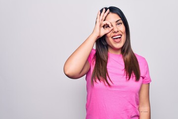 Young beautiful brunette woman wearing casual pink t-shirt standing over white background doing ok gesture with hand smiling, eye looking through fingers with happy face.