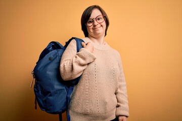 Young down syndrome student woman wearing school bag over yellow background with a happy face standing and smiling with a confident smile showing teeth