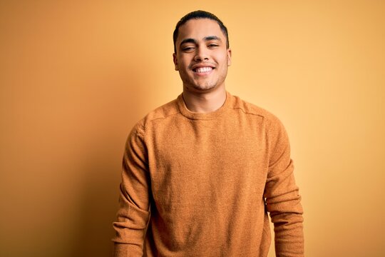 Young brazilian man wearing casual sweater standing over isolated yellow background with a happy and cool smile on face. Lucky person.