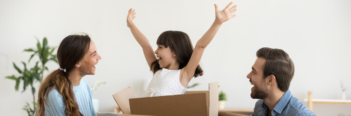 Daughter jumps out of box at moving day at new home with loving parents, family have fun unpack...