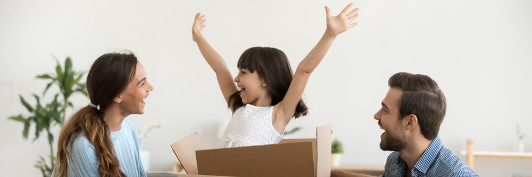 Daughter jumps out of box at moving day at new home with loving parents, family have fun unpack their belongings start new life at first house concept horizontal photo banner for website header design