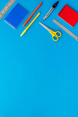 School supplies pattern - notebook, pen, ruler, sciccors - on blue table top-down copy space
