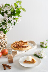 Homemade seasonal french apple pie - galette with ripe apples, cinnamon and honey. Baked galette with apples and spices on a lining and blossom branches. Side view. Bakery menu. Copy space