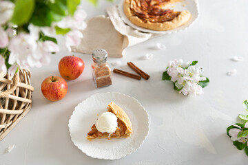 Piece of Homemade seasonal french apple pie - galette with ripe apples, cinnamon and ice cream. Baked galette with apples and spices on a lining and blossom branches. Side view, close up.