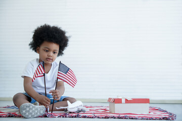 African American boy holding little usa flags sitting on us blanket on white background,...