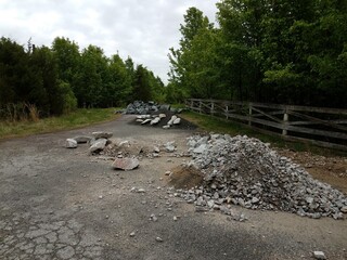 asphalt street with piles of grey rocks or stones and trees