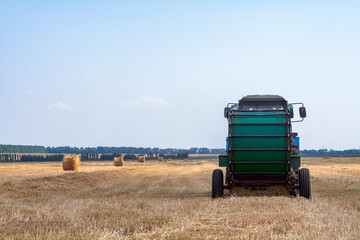Obraz premium A tractor with a trailed bale making machine collects straw rolls in the field and makes round large bales