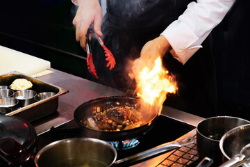 Chef cooking with flame in a frying pan on a kitchen stove.