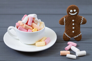 Cup with colored marshmellow and smiling gingerbread man close-up on wooden gray background. Christmas sweets concept